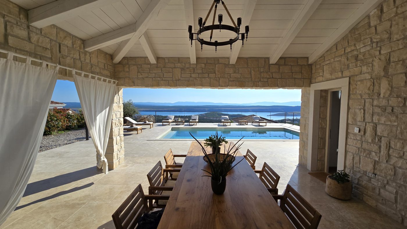 Covered terrace with a dining table framing the pool and the sea