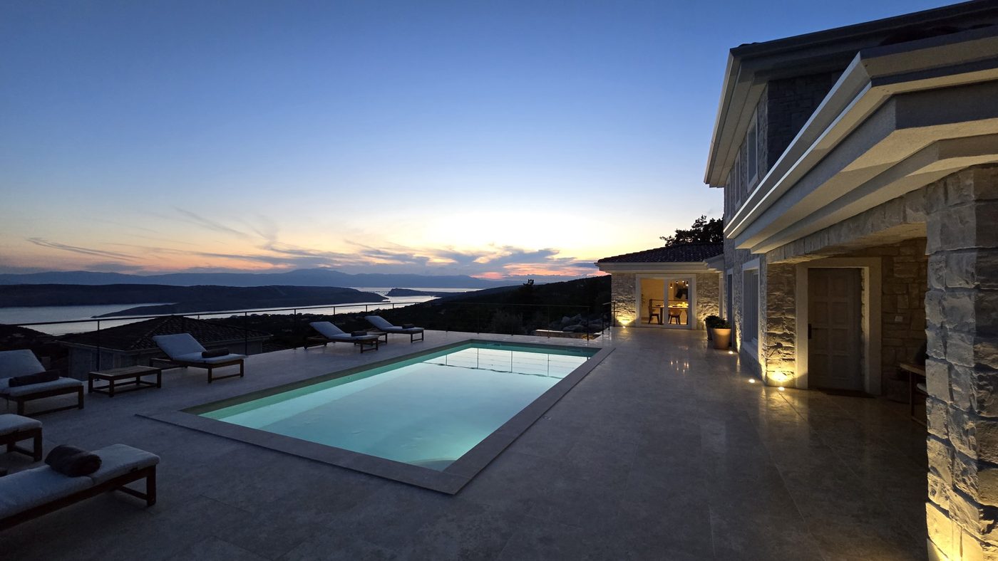 The villa and pool lit at dusk with the bay behind